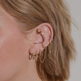 Up close ear stack with multiple piercings, using small hoops and gold pave huggies for curated look climbing the ear. 