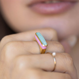 Model wearing gold ring with wide turquoise quartz stone and pink enamel band around stone